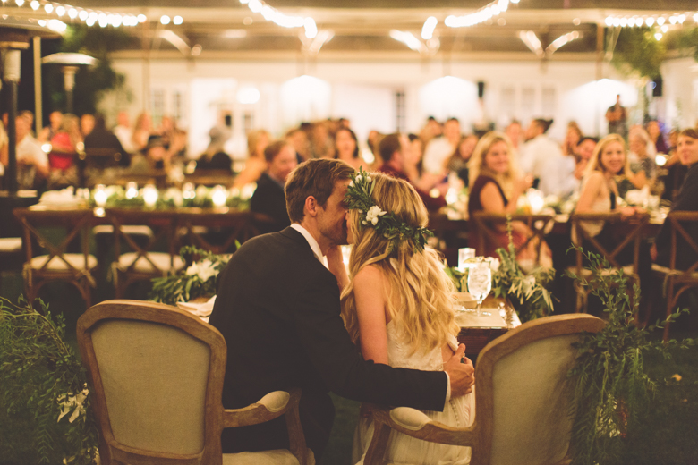 Photo of Tyler Hilton and Megan Park kissing at their wedding table.