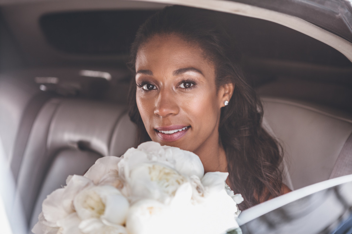 A close up of a bride with her bridal bouquet through a car window.