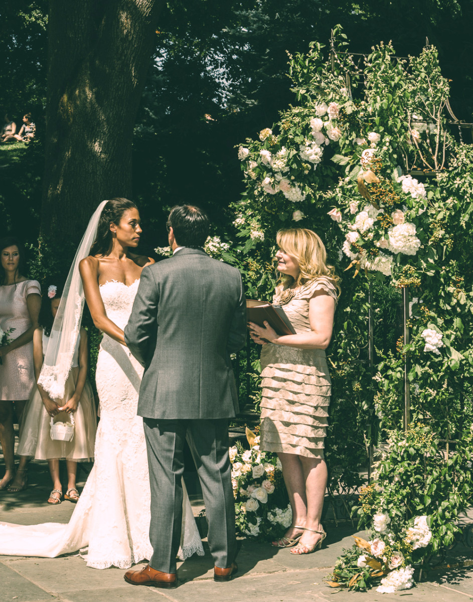 A couple is married in the park in front of a floral archway.