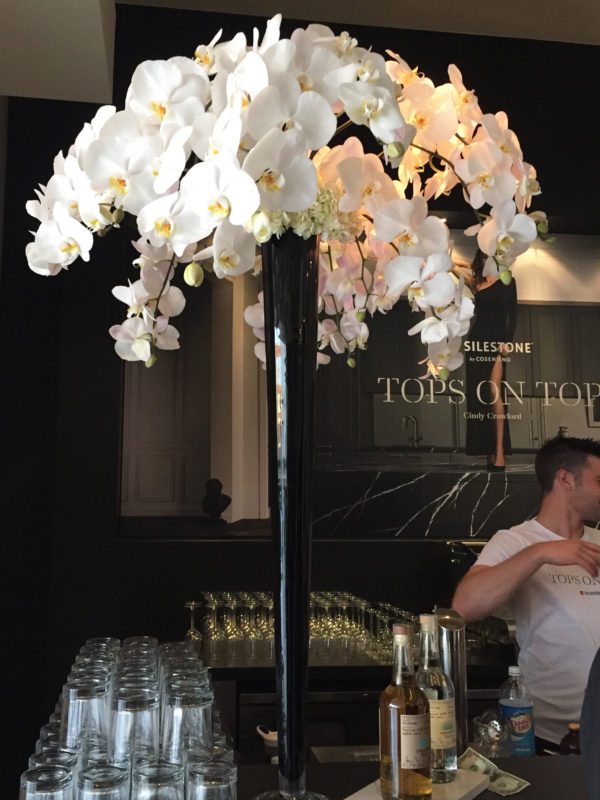 A tall white orchid arrangement in a black vase sits atop a bar at a Cindy Crawford & Silestone® event in Hollywood, CA.